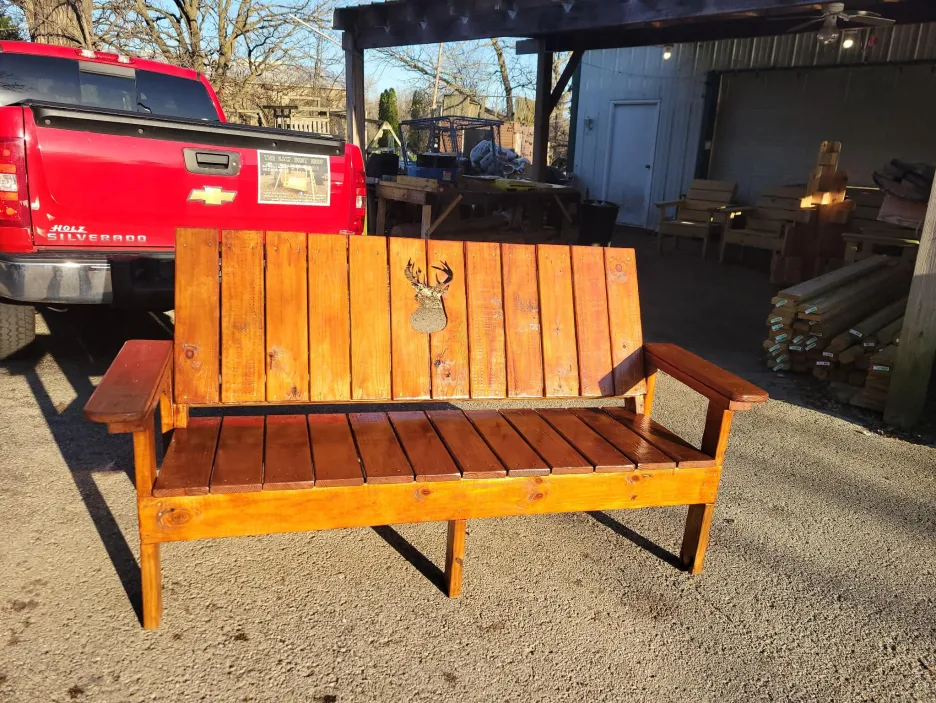 Stained wooden outdoor bench with decorative deer cutout in the backrest and wide armrests