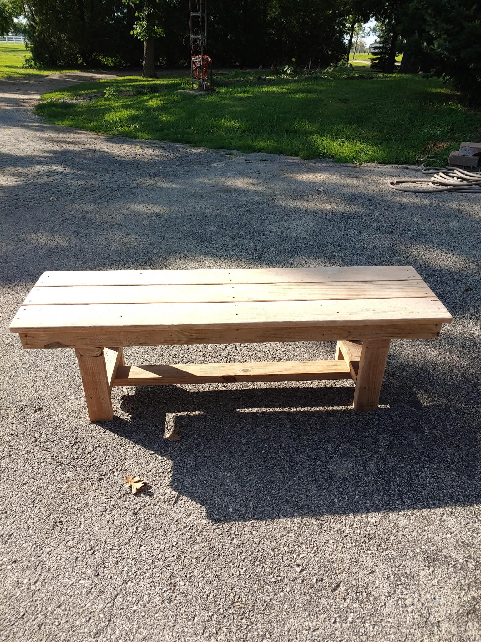 Simple unstained outdoor wooden bench with clean plank top and lower crossbar