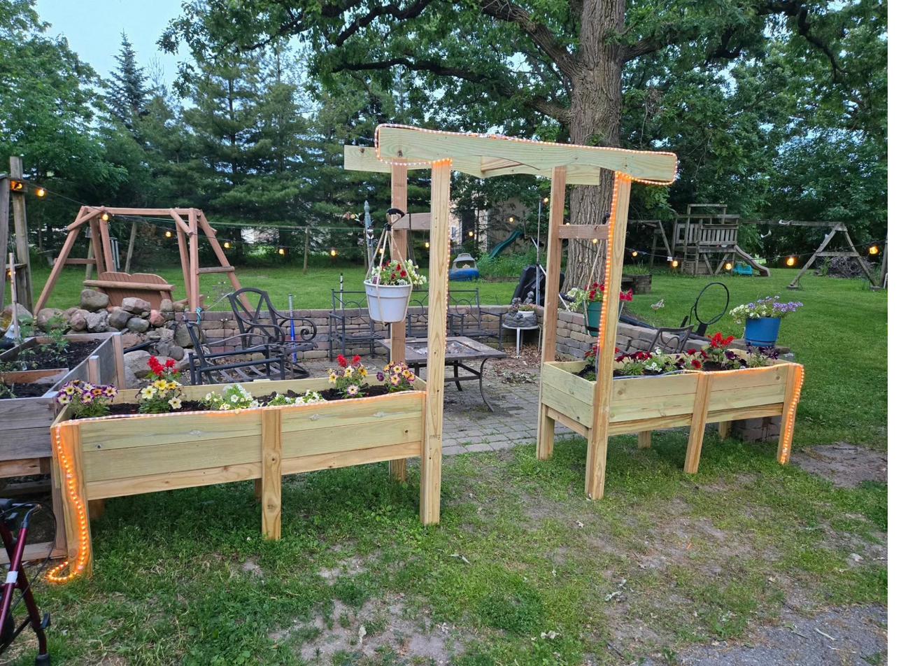 Raised wooden garden boxes with arch trellis and string lights, planted with colorful flowers